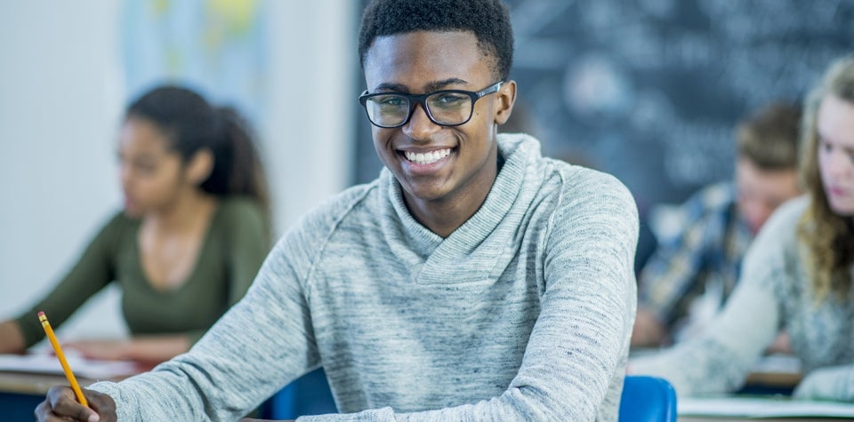 Image of a young man in a classroom smiling up at the camera.