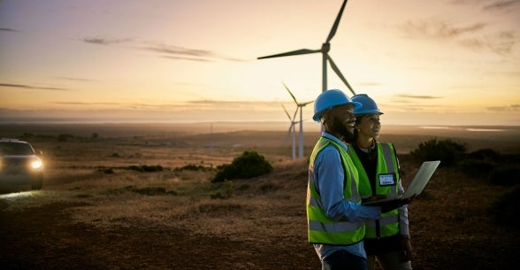 Sustainable Future: ESG Leadership in Action - Workers in reflective vest holding a laptop computer - Windmills in the background sunset horizon