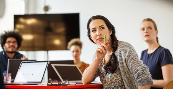 Image of diverse workers in a meeting with their laptops, looking at something just off screen.