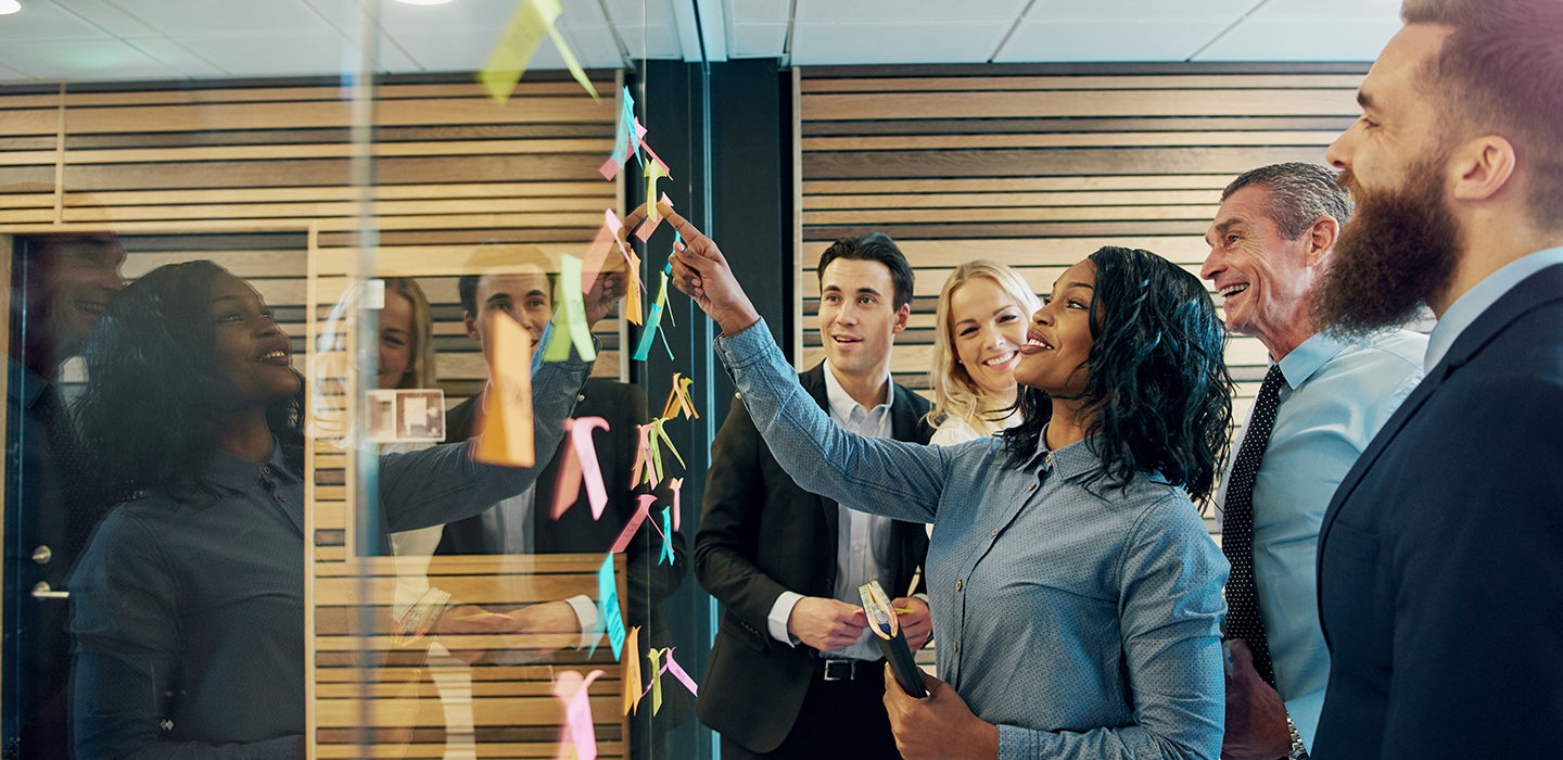 Image of office workers smiling up at a board of post it notes