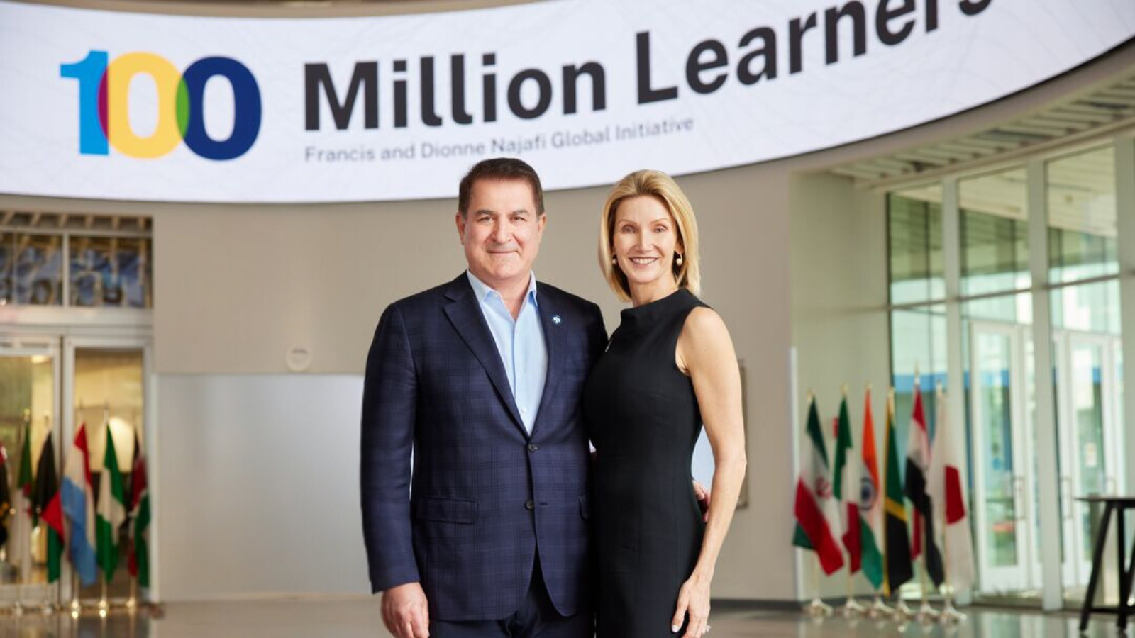 Francis and Dionne Najafi pose together under the sign for the "100 Million Learners" Francis and Dionne Najafi Global Initiative.