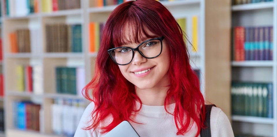 Изображение молодой женщины в очках, стоящей в библиотеке.