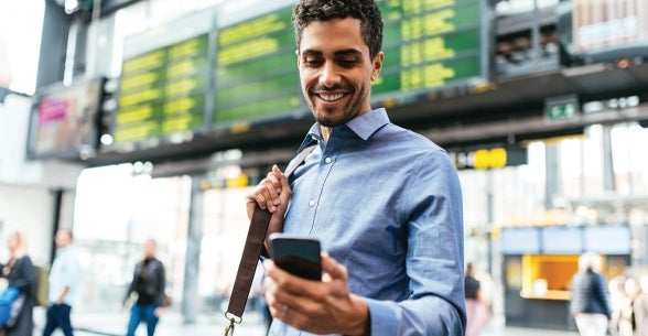 Image of a man in business attire looking at his phone and smiling while in an airport.