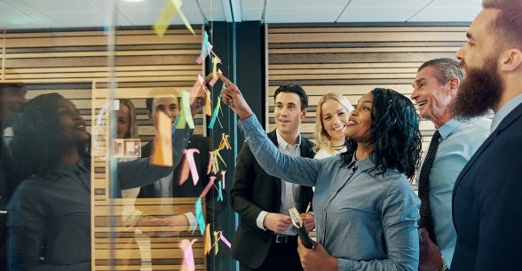 Image of office workers smiling up at a board of post it notes