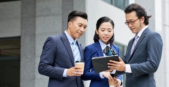 Group of three business people looking at a tablet.
