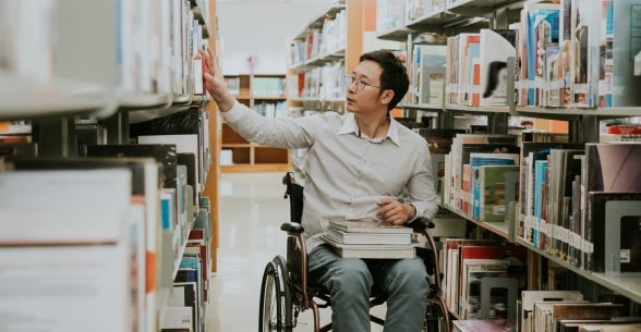 A student in a wheelchair examines library stacks.
