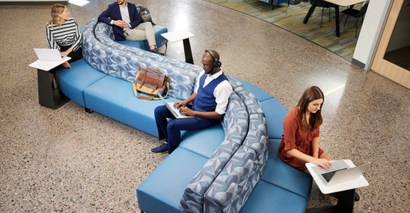 People working while sitting on a wavy couch in a lobby.