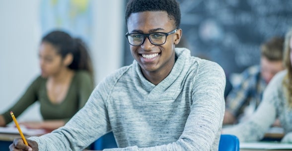 教室でカメラに向かって微笑む若い男性の画像。